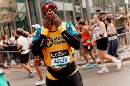 Serge Nguélé approaching the finish line of the 2025 TCS London Marathon, hands clasped in gratitude, marathon bib 44229 visible