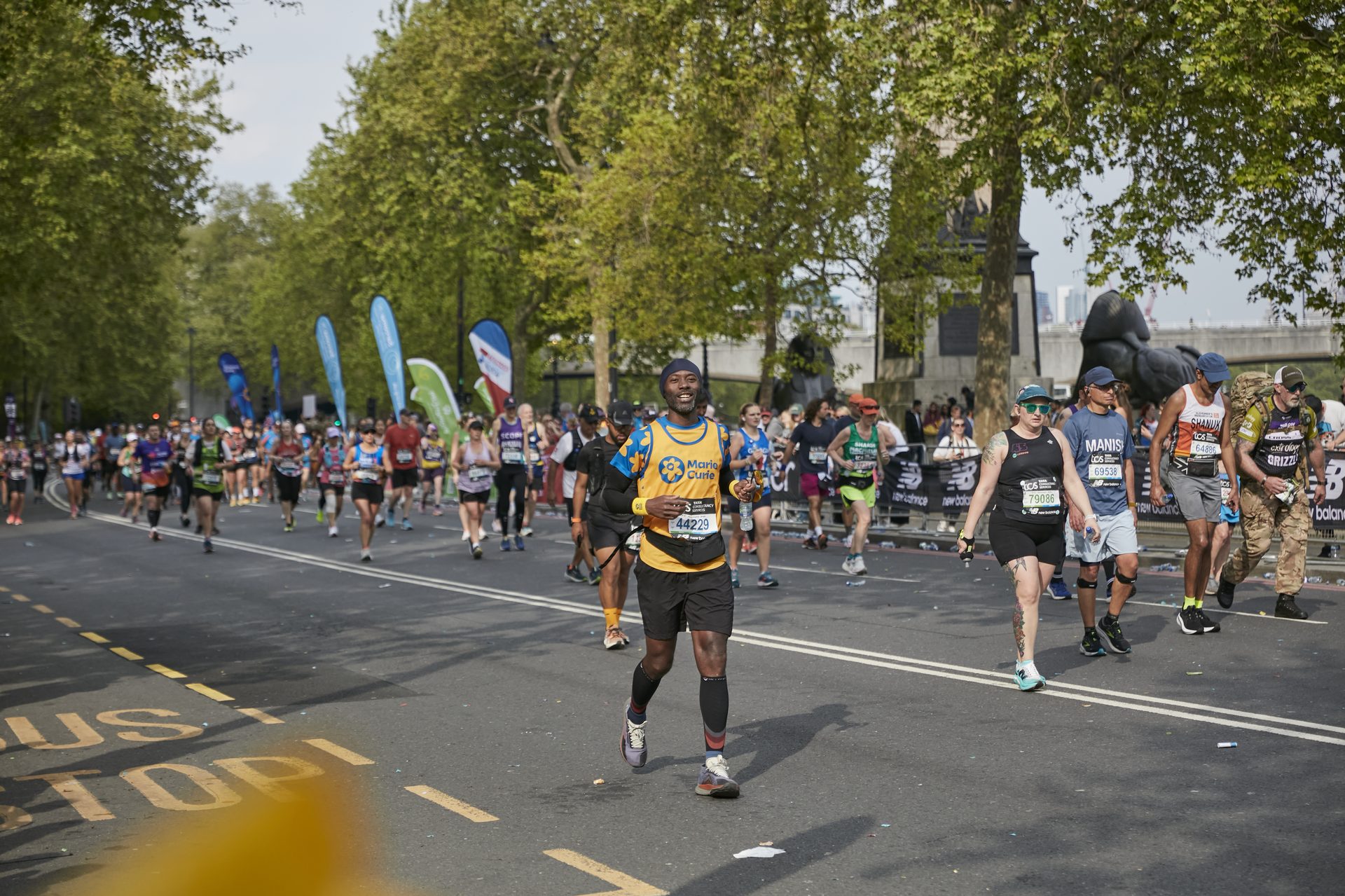 Serge Nguélé running the 2025 TCS London Marathon for Marie Curie, arms outstretched mid-stride, wearing the Marie Curie charity vest with bib number 44229